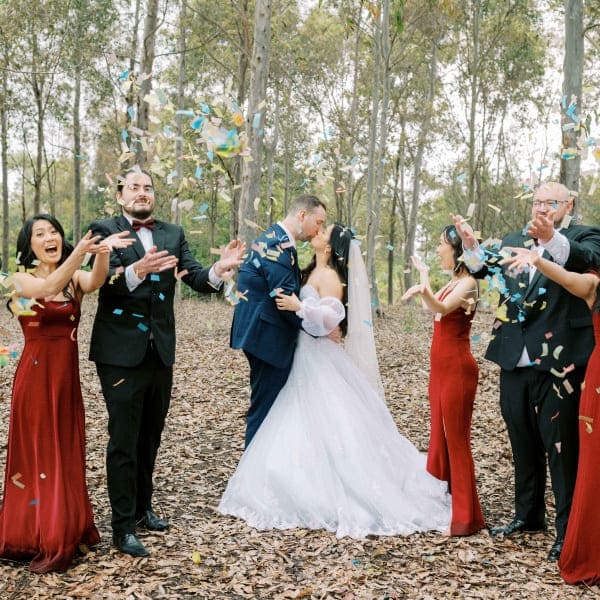 Bride and groom kissing while bridal party throws confetti