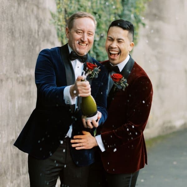 Two grooms celebrating their marriage with a champagne pop